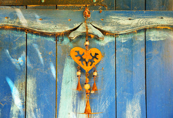 Close-up of an old wood door painted in bright blue with a rusty iron heart shape decoration hanging, Italy 