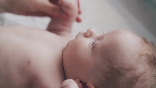 cute newborn son with short fair hair and adorable plump cheeks lies on changing table and moves body extreme close view