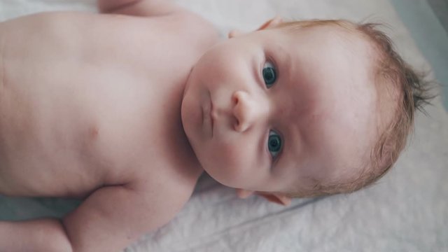 infant boy with short blond hair and large crystal blue eyes lies on changing table and looks at camera extreme closeup