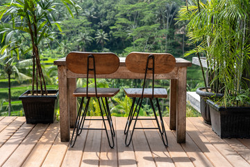 Wooden table and chairs in empty tropical cafe next to rice terraces in island Bali, Indonesia