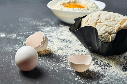 Dough in firepan with flour near different utensils and ingredients lies on dark concrete table. Baking process. Copy space
