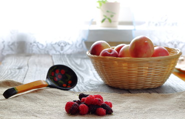 Basket of peaches, mulberries, raspberries and painted spoon on a wooden table