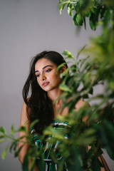 Fototapeta premium Close up portrait of a beautiful, young, elegant and sexy Indian Asian woman in a classy outfit. She is tall, beautiful and projects confidence and class as she stands behind a plant at home. 