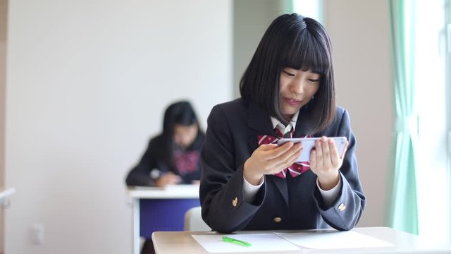 High school girl looking at smartphone and smiling in classroom