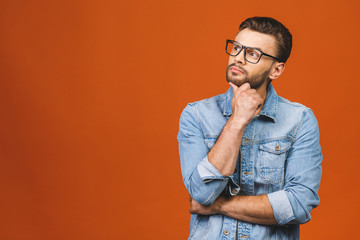 Happy young man. Portrait of handsome young man in casual shirt keeping arms crossed and thinking while standing against orange background.