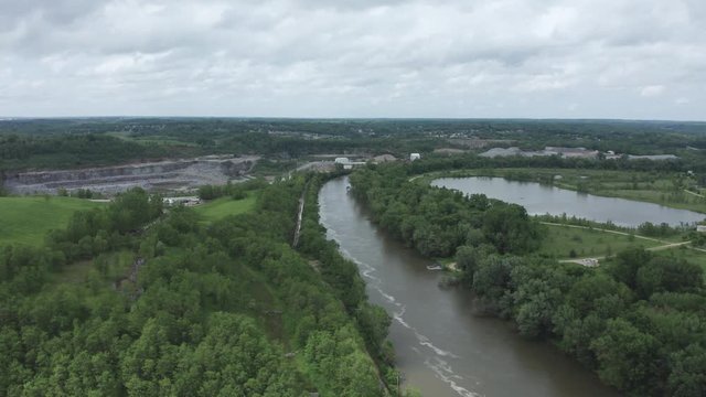 Drone flies over a rolling river, over a forest, to a quarry in the Midwestern USA.  in summer, in 4K.