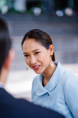 Close up portrait of a beautiful, elegant, confident and attractive young Chinese Asian woman in a blue suit talking to a friend, a colleague or a recruiter during the day. She is smiling.