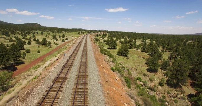 Aerial pull away from a single man standing along the parallel train tracks​ near Williams, Arizona. Concept: Southwestern US, railroad, ​transportation
