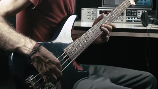Musician records a bass guitar track in his own studio.