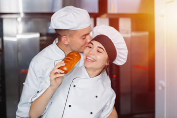 Boy baker kisses a girl on the cheek in a bakery against the background of the oven.