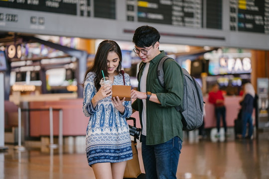 Portrait of a young Asian interracial couple (Korean man and his Indian girlfriend) checking their passports and tickets in an airport. They are smiling excitedly for their holiday trip / vacation.