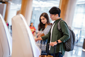 A portrait of a pair of young and excited Asian travelers (Korean man and his Indian friend) checking in to board their plane for their holiday at an automated check-in booth in the airport.