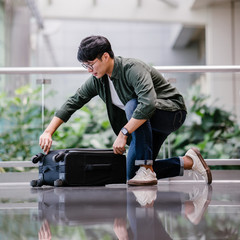 Portrait of a handsome, young and attractive Korean Asian man is kneeling and packing his luggage...