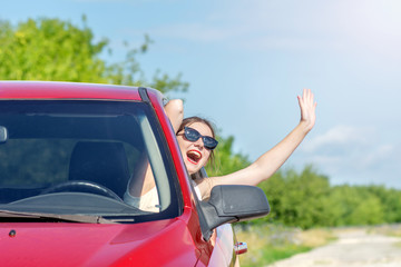 office young happy woman leaning out of open car window laughing with outstretched arms.