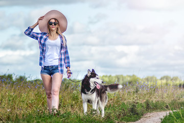 Naklejka na ściany i meble happy beautiful girl in the blooming field walk with siberian Husky, enjoying dog and sun