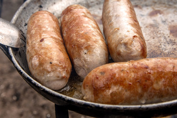 Grilled sausages on pan grill with smoke and flame on a meadow. Barbecue picnic concept