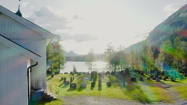 Beutiful and dreamy reveal shot of lake and norwegian nature, behind a church over a litte smal graveyard