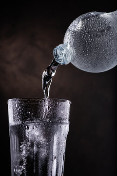 fresh water poured from plastic bottle into glass beaker on the dark background