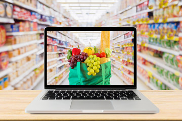 supermarket aisle blurred background with laptop computer and green shopping bag on wood table...