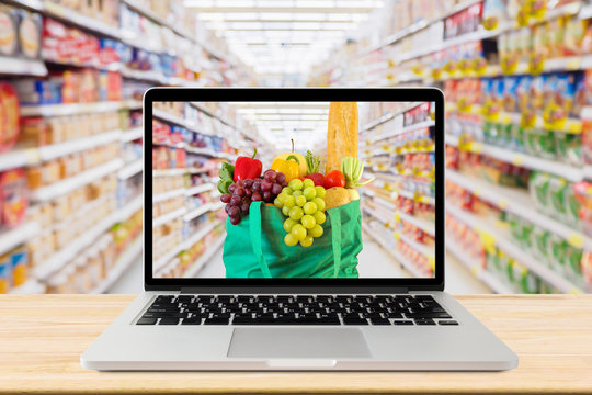 supermarket aisle blurred background with laptop computer and green shopping bag on wood table grocery online concept