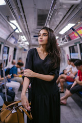 Portrait of a tall, slim, beautiful and attractive Indian Asian woman riding the train on her own with her luggage. She is heading to the city from the airport. She is wearing a casual black dress.