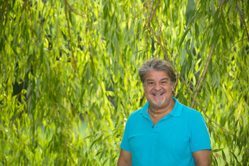 Man poses for a portrait in the shade of a tree. He is smiling and looking to the camera.