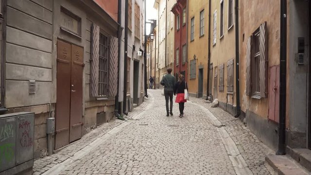 Couple walking narrow streets in city holding hands. Man & woman walking down alley holding hand.