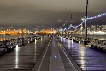 Pier decorated with Christmas flags in rainy weather against the background of the port and downtown of Vancouver, the beautiful  reflection of lights on the wet surface of pier