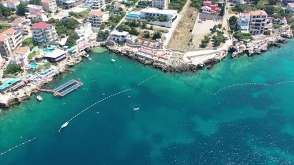 Flying from sea to the beach. Water in the sea is turquoise, clean and clear. Drone flies to the stone sea beach with its multicolored umbrellas and beach loungers. White boats near the shore