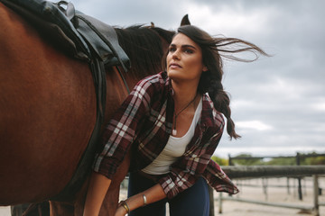 Young woman saddling the horse