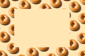 Bagels pattern on a peach color background with a rectangular frame in the center for your text. Bakery product template, traditional Russian bread product. Creative layout. Top view. Copy space