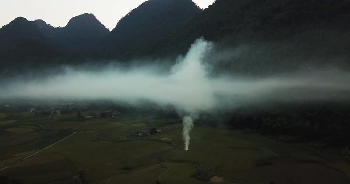 Moody landscape with mountains over the clouds. Dark orbiting, aerial shot above hidden village with smoke rising up from burning fields,Lam Thuong valley, Vietnam