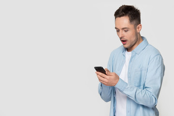 Amazed shocked man holding phone pose over studio grey background