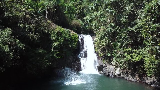 Still Drone Shot from one of the AlingAling Waterfalls in Bali, Indonesia. A man can be seen jumping and doing a gainer flip off of the cliff into the pool of water.