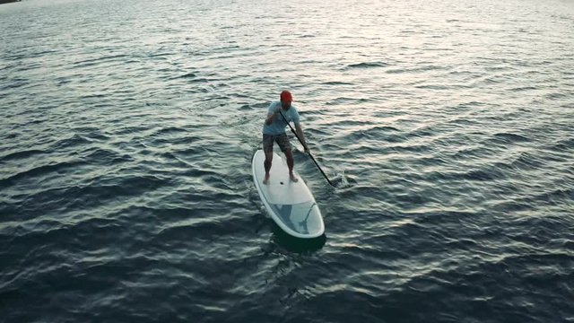 Caucasian man paddleboards fast on small waves. Pan from in front of the board.
