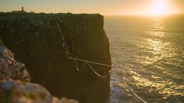 Stunning static shot of a slackliner making his way across a line while the sun sets over the ocean
