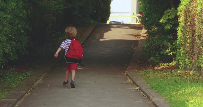 A cute little boy turns and runs off down the sidewalk to school