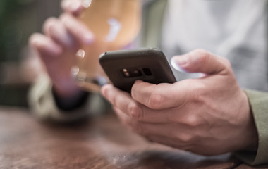 close up of man hand hold smartphone, drinking beer and reading message at bar or pub