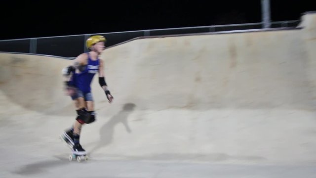 Quad skater does a seated drop-in into a bowl and skates back and forth at night