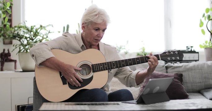 Mature adult female learning to play the guitar at home with a video tutorial