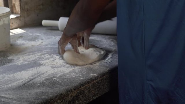 Baker put flour on the table from the bucket, turn over dough in flour and use roller pin