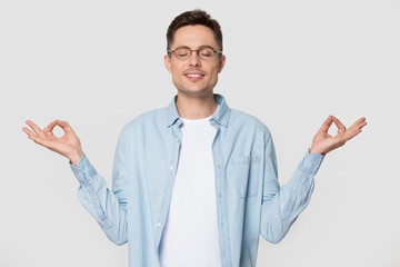 Young man makes mudra gesture meditates standing over grey background