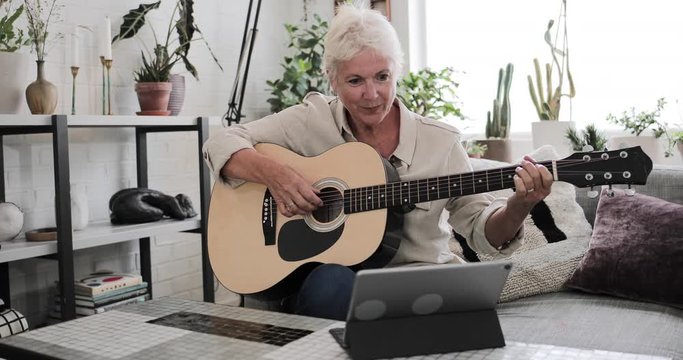 Mature adult female learning to play the guitar at home with a video tutorial