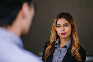 A young, beautiful and attractive Southeast Asian woman in a suit is smiling as she talks to a Chinese man in the city during the day. She is tanned and confident and looks focused on the conversation