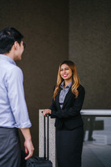 A young, tanned, beautiful and confident Asian business woman in a business suit smiles and shakes hand in agreement to mark a deal with an Asian man. They are standing in an Asia city during the day.