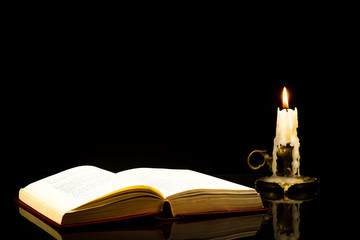 An open book isolated on a black background with a candle in the background