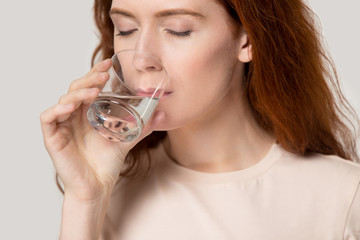 Close up young thirsty red-headed woman drinking clean water