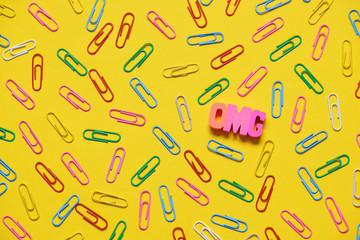 Colorful paperclips on yellow background and omg letters