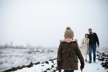 Happy family walk on the snow road. Mom, dad, daughter stand outdoors on the background winter.