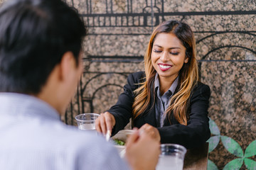 Portrait of two diverse Asian colleagues having a business lunch together. A tanned and attractive young Malay Asian woman is enjoying her salad as she talks to her Korean companion over lunch.